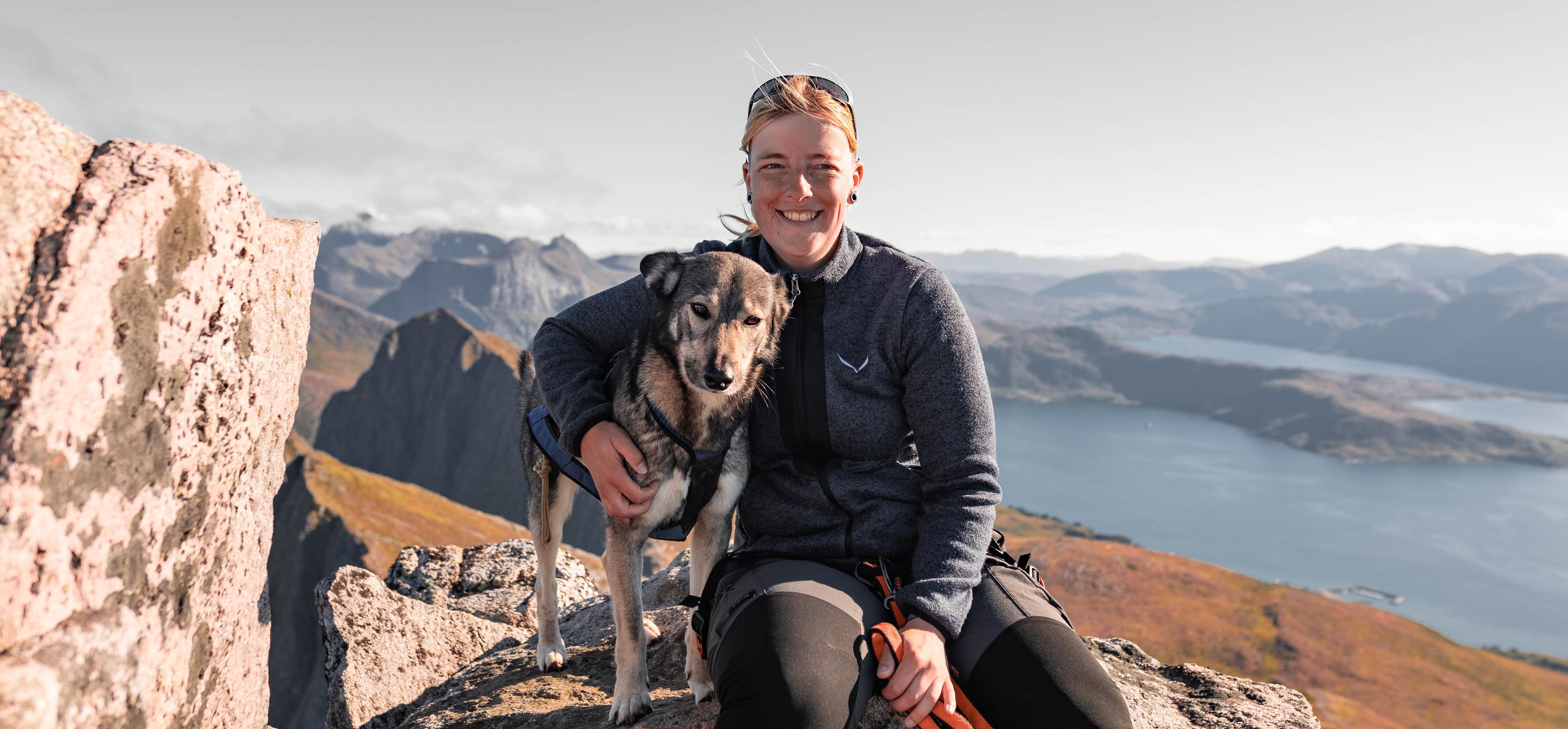 Anne sitting with her dog on a mountain hike in Senja, Norway, representing experience with navigating real terrain and complex AppSec programs.