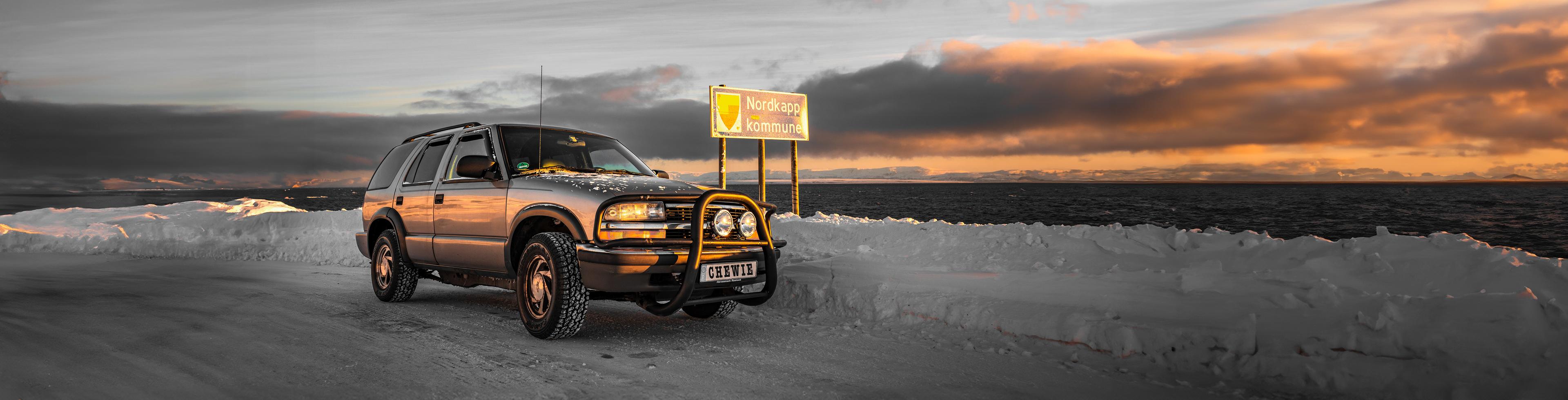 1999 Chevy Blazer parked next to the Nordkapp kommune sign on a snowy road at sunset in winter.