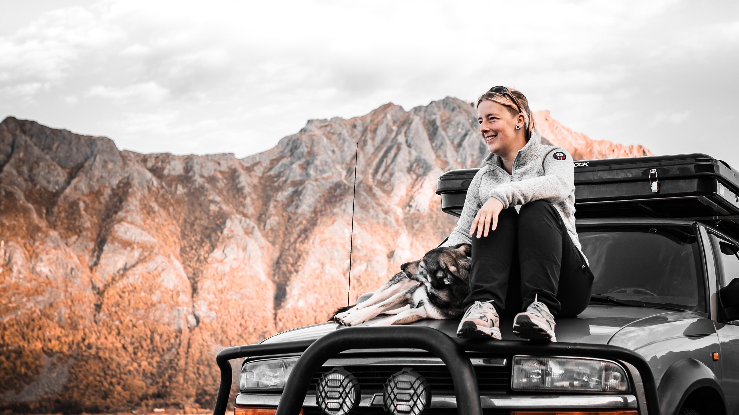 Anne sitting on Chewie with her dog, overlooking the mountains on Lofoten Islands – living the overlanding life.