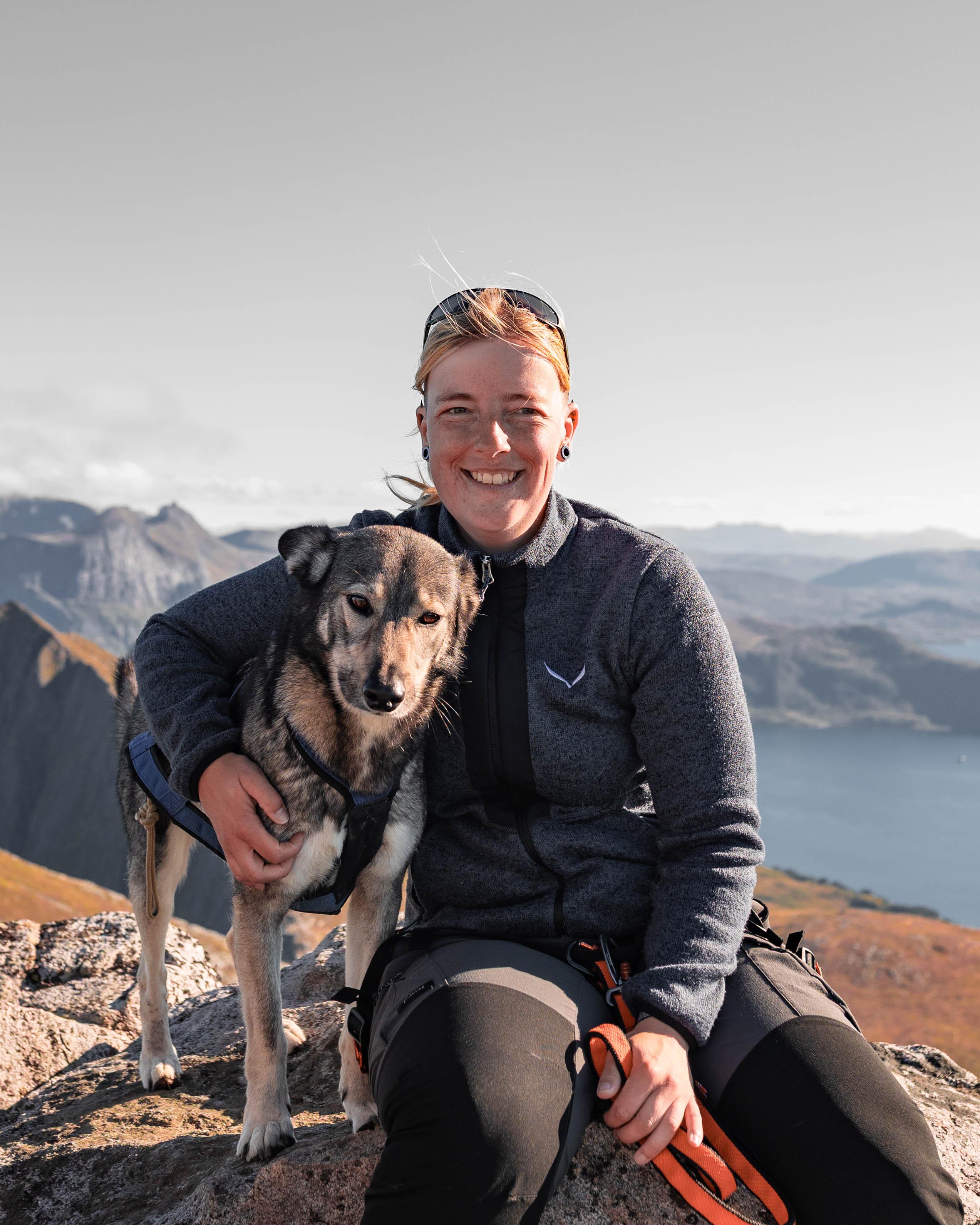 Anne sitting with her dog on a mountain hike in Senja, Norway, representing experience with navigating real terrain and complex AppSec programs.