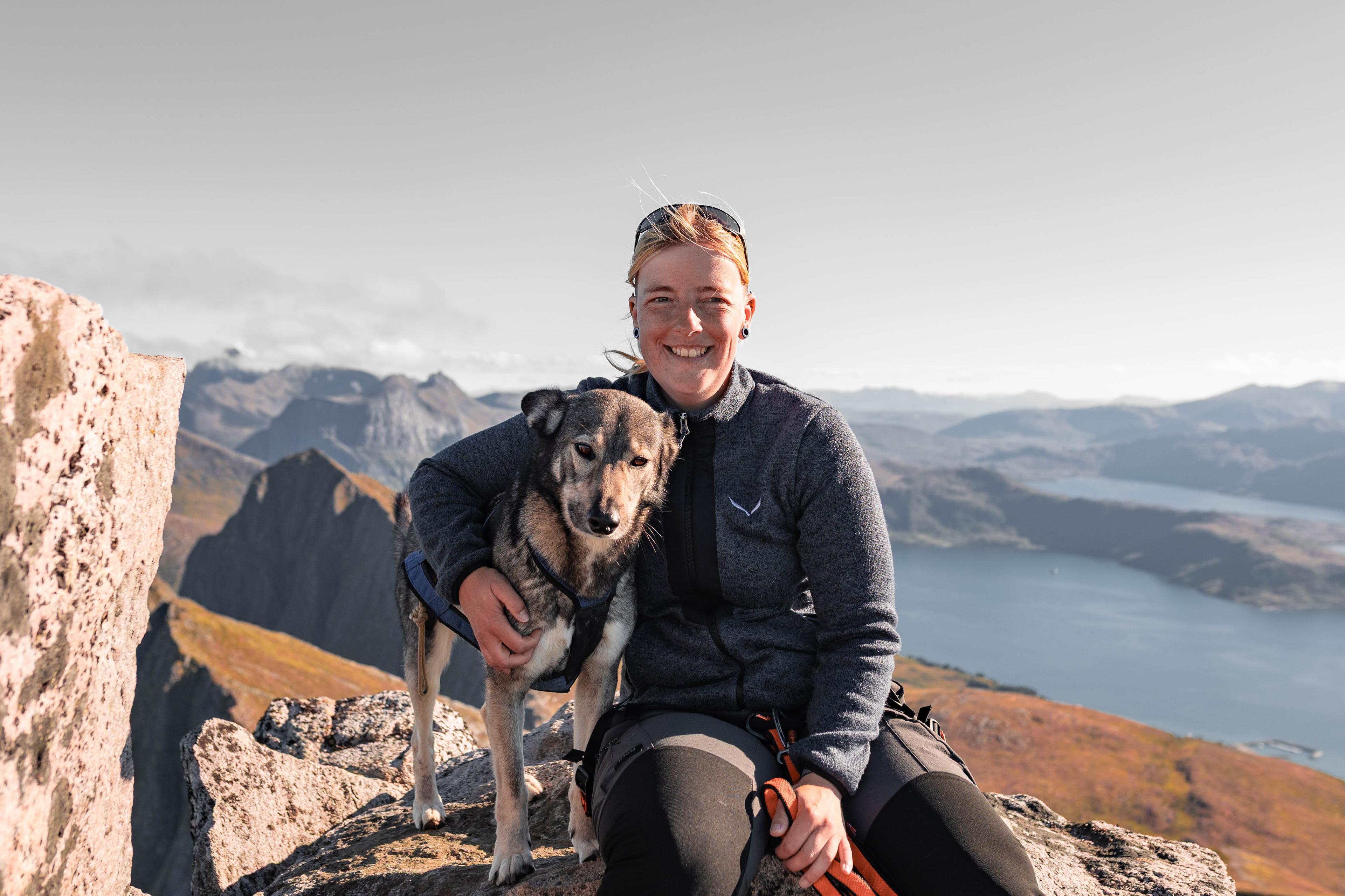 Anne sitting with her dog on a mountain hike in Senja, Norway, representing experience with navigating real terrain and complex AppSec programs.