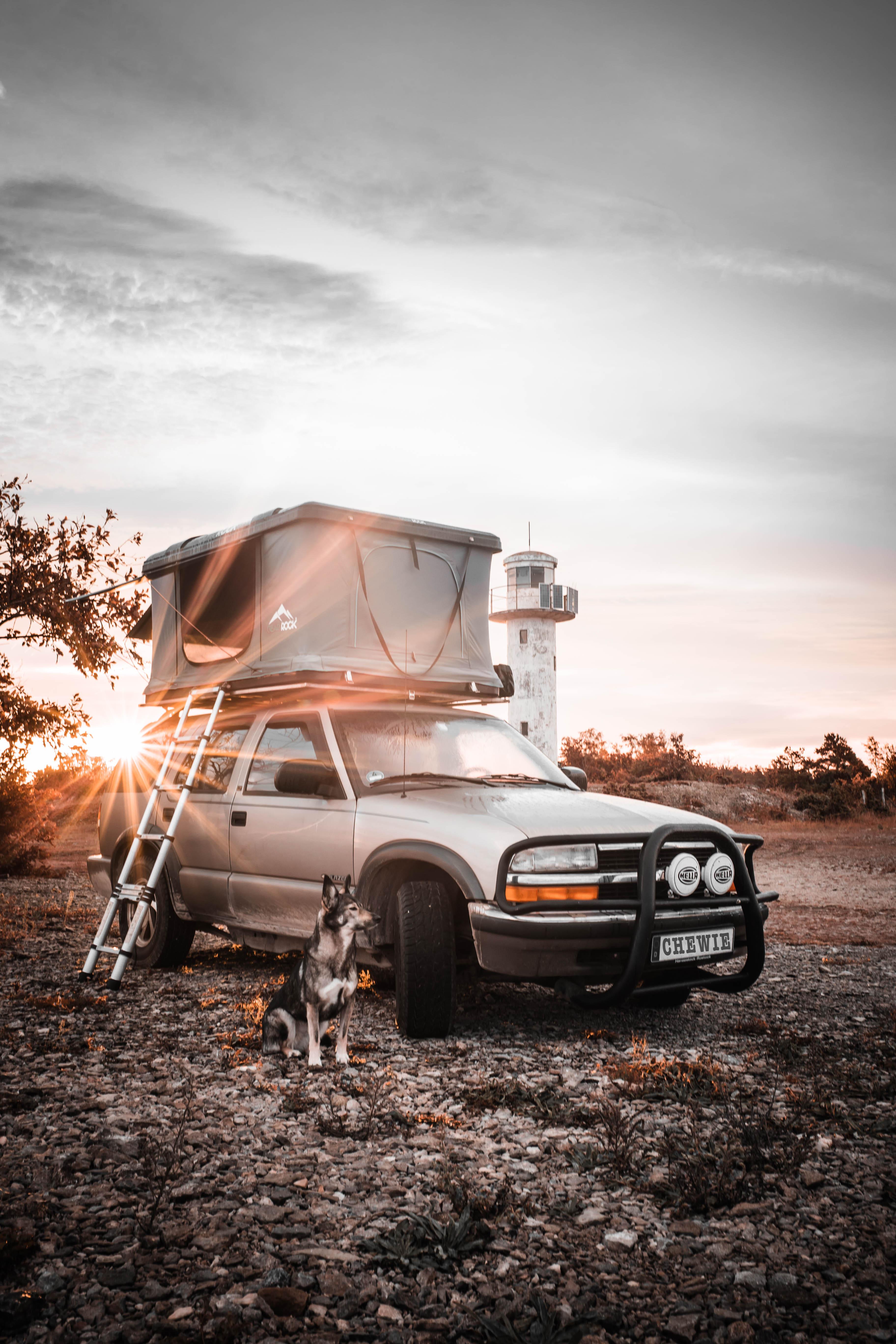Chevy Blazer with rooftop tent and dog, parked near a lighthouse at sunset – ready for the next mission.