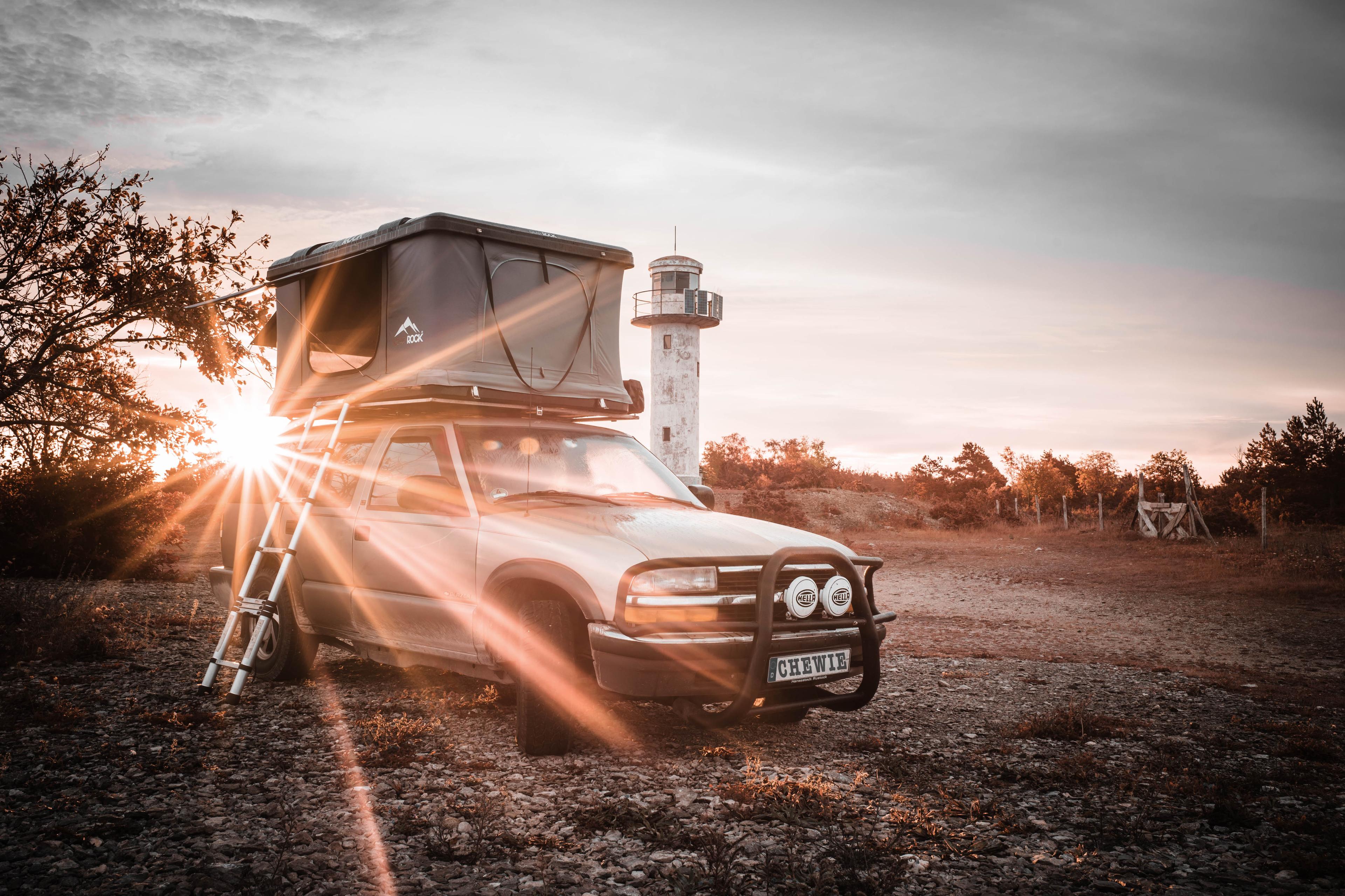 Chevy Blazer with rooftop tent and dog, parked near a lighthouse at sunset – ready for the next mission.
