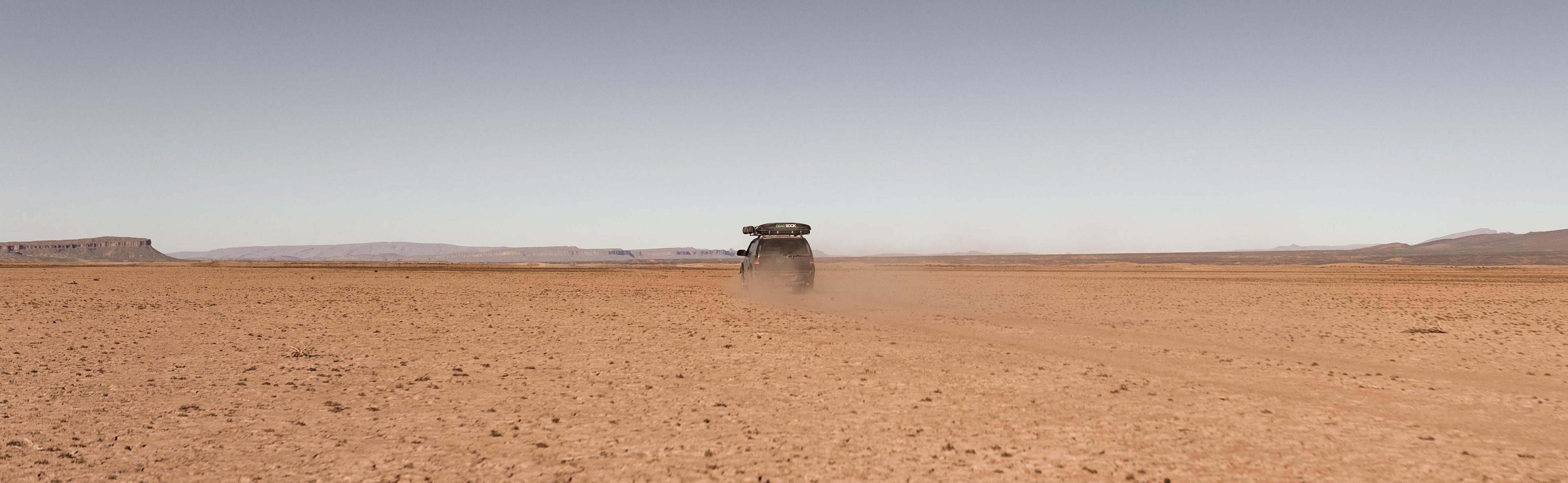1999 Chevrolet S10 Blazer driving across the dry bed of Lake Iriki in Morocco with a dust cloud behind it.