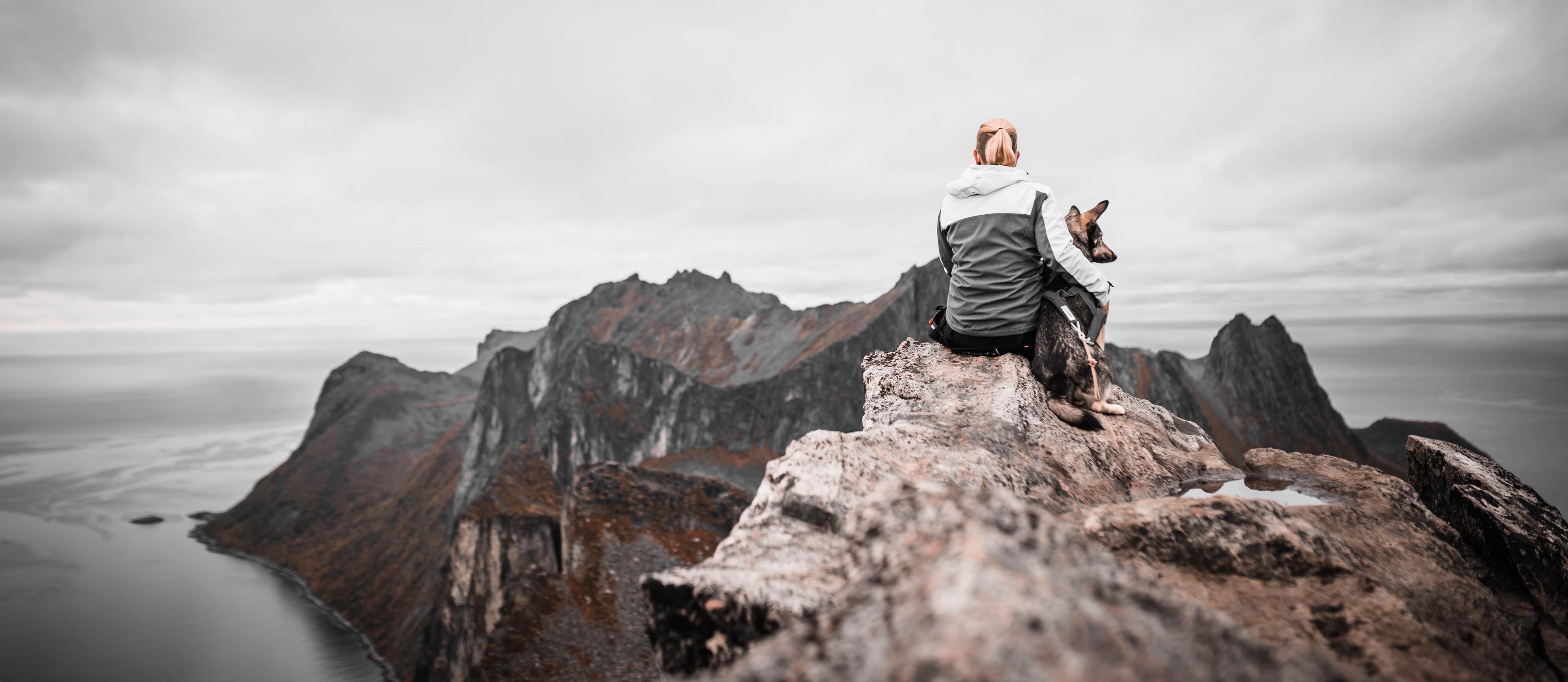 Anne and her dog on Segla mountain in northern Norway Anne and her dog sitting on top of the Segla mountain in northern Norway, overlooking a dramatic coastal landscape that reflects the Trail Guide theme of guidance and direction.